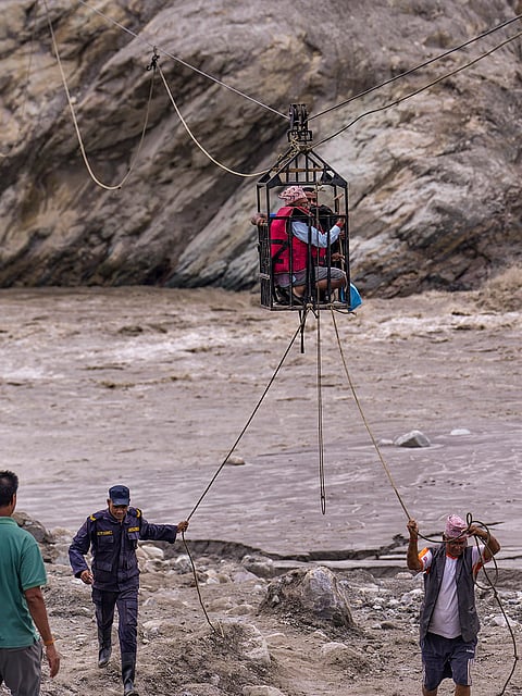Workers pull ropes as people use a makeshift zipline to cross the Trishuli river from Koloni in the aftermath of the recent flash floods, in Nuwakot district, Nepal.