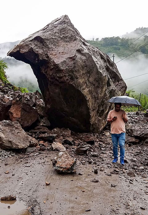 A commuter walks past a massive boulder that fell onto the Nandanagar-Nandprayag road, completely blocking traffic following heavy rainfall and a subsequent landslide, in Chamoli district, Uttarakhand,