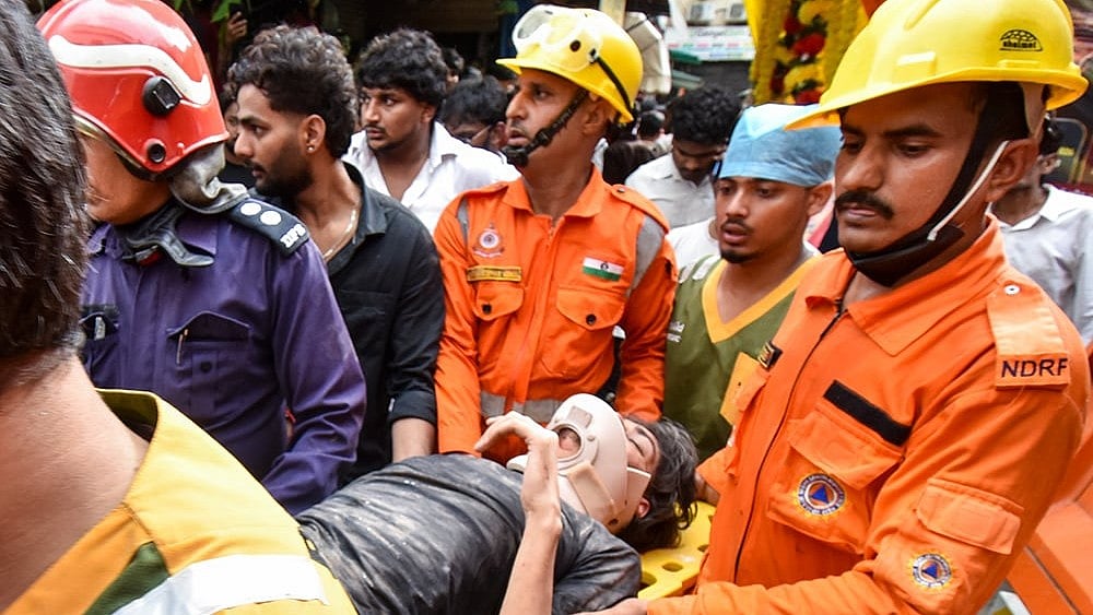 Delhi Building Collapse LIVE: NDRF, fire department officials carry a rescued person after a 50-year-old five-storey building housing a boys' hostel collapsed in a congested bylane in Satya Niketan near Delhi University’s south campus. Three died in the incident. - | Photo: PTI