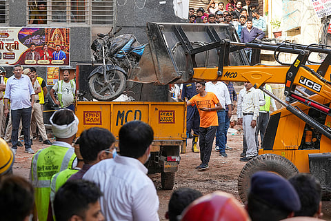 An excavator moves a damaged two-wheeler vehicle during a rescue operation on the second day after a 50-year-old five-storey building housing a boys' hostel collapsed in a congested bylane in Satya Niketan near Delhi University’s south campus. The death toll in the building collapse in southwest Delhi's Satya Niketan area climbed to six.