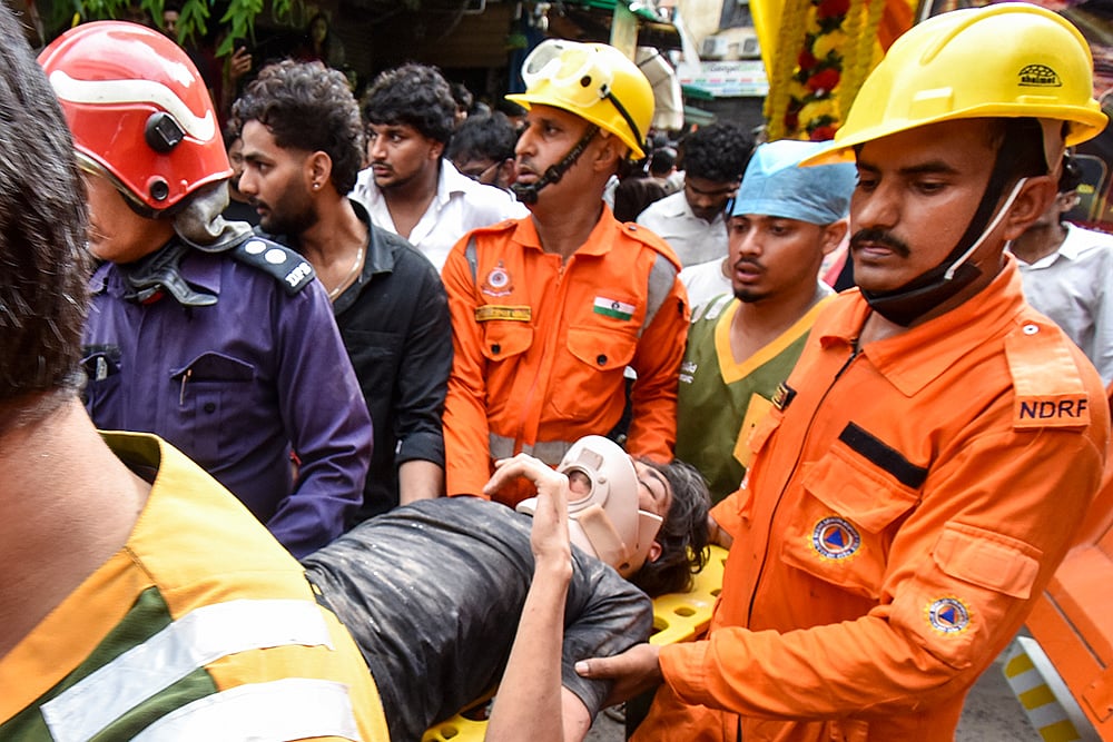 | Photo: PTI : NDRF, fire department officials carry a rescued person after a 50-year-old five-storey building housing a boys hostel collapsed in a congested bylane in Satya Niketan near Delhi University’s south campus. Three died in the incident.