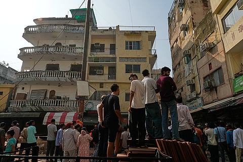 People watch as rescuers clear debris at the site of a collapsed building in New Delhi, India.
