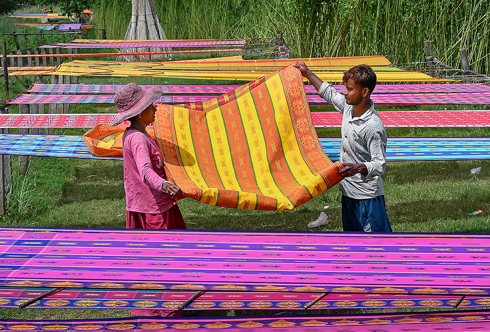Workers dry handloom clothes at a field