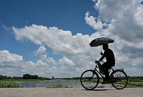 A man rides a bicycle along a road as he covers himself on a cloudy day, in Nadia district, West Bengal.
