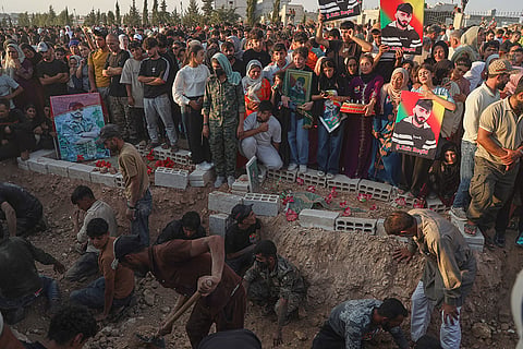 Mourners holding portraits gather beside graves during a mass funeral for prisoners who died in a fire that broke out during unrest at the local prison in the predominantly Kurdish city of Kobani, northern Syria.