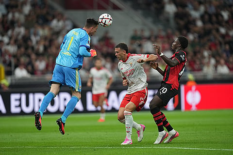 Benfica's goalkeeper Anatoliy Trubin heads the ball as AC Milan's Alphadjo Cisse and Benfica's Alessandro Circati watch the ball during the Europa League opening phase soccer match between AC Milan and Benfica in Milan, Italy.