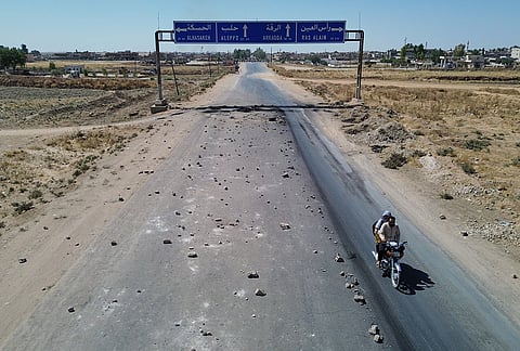 Two men ride a motorcycle through an improvised roadblock set up by local residents to stop oil tankers from the Rmeilan oil fields during ongoing protests against higher fuel prices near Tal Tamr in northeastern Syria, Wednesday, Sept. 16, 2026. 