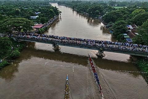People stand on a bridge over the Kulsi river to watch men compete in a traditional boat race in Champupara village, west of Guwahati, India.