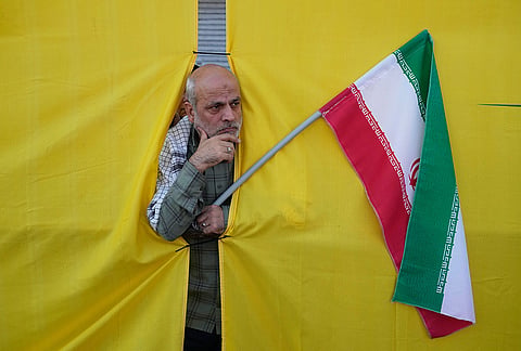 A man holding an Iranian flag peers through an opening in a curtain during the state-organized “Janfada,” or “Sacrifice for Iran,” military-style parade in Tehran, Iran, Friday, Sept. 18, 2026. 