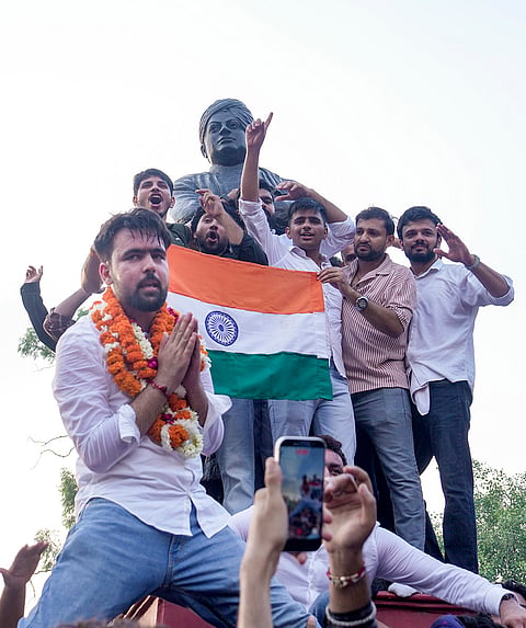 Independent candidate Deepanshu Shokeen, garlanded, celebrates with others atop Swami Vivekanand's statue after winning the vice-president's post in the Delhi University Students' Union (DUSU) elections, at North Campus, in New Delhi, Saturday, Sept. 19, 2026. 
