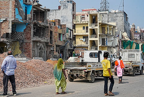 People gather at the site following a demolition drive carried out by civic authorities on Max Hospital Road as part of a road-widening project, at Shalimar Bagh area, in New Delhi.