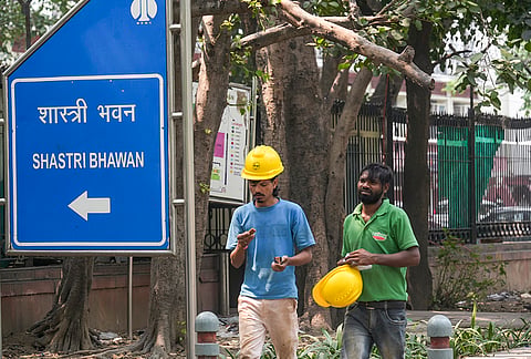Construction workers walk past a signboard of Shastri Bhawan after the Central Public Works Department (CPWD) initiated the process to vacate the building by the end of September ahead of its planned demolition to make way for new 'Kartavya Bhawan' blocks under the Central Vista redevelopment project, in New Delhi.