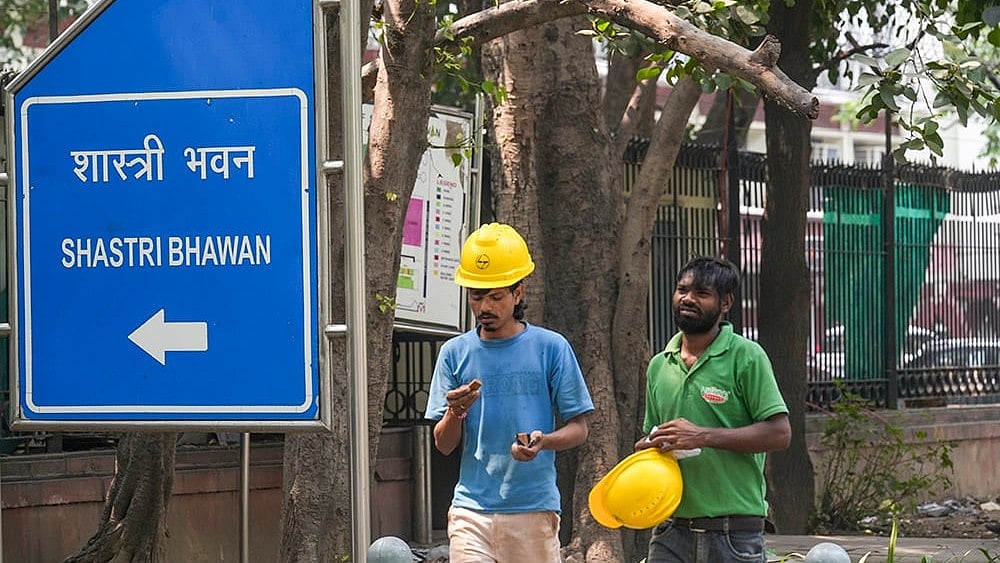 Construction workers walk past a signboard of Shastri Bhawan after the Central Public Works Department (CPWD) initiated the process to vacate the building by the end of September  - | Photo: PTI/Karma Bhutia