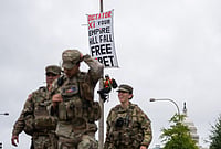 | Photo: AP/Allison Robbert : A protester scales a light pole and unfurls a banner to protest the upcoming State Visit by China's President Xi Jinping as members of the National Guard walk by, Tuesday, Sept. 22, 2026, in Washington. 