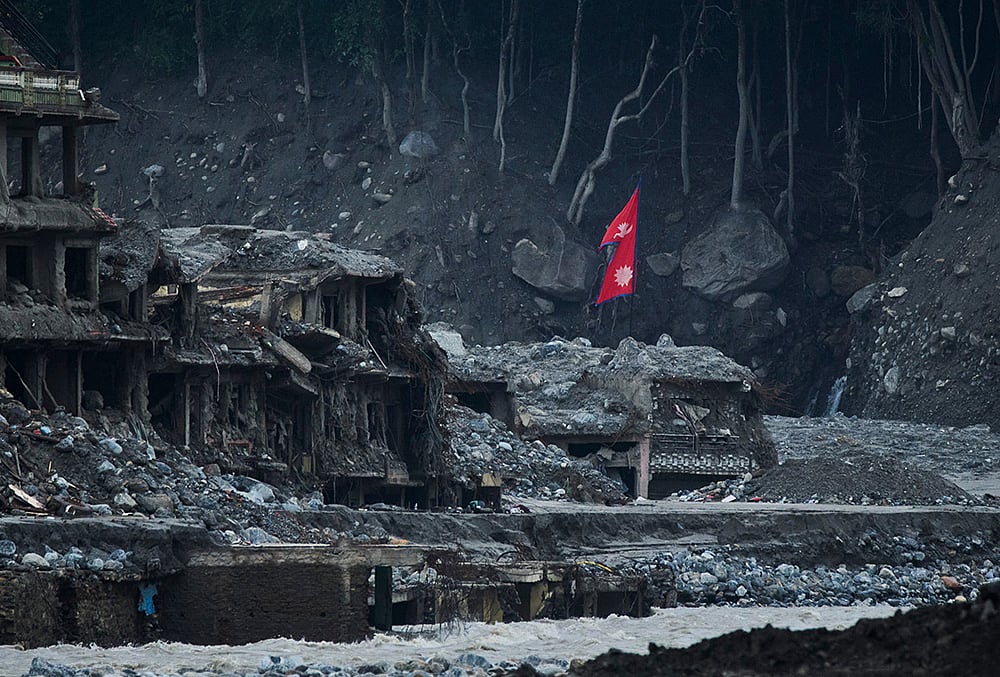 A Nepalese flag flies amid houses damaged by flash floods along the banks of the Trishuli River in Dunge, in Nepal's Nuwakot district, Wednesday, Sept. 23, 2026.  - | Photo: AP/Niranjan Shrestha