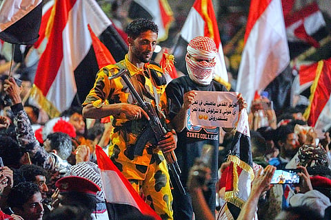 A Yemeni soldier stands alert as a man holds a message to Houthis that reads in Arabic, "the road to Jerusalem does not pass through Taiz," during a celebration of the 64th anniversary of the September 26 Revolution in Taiz, Yemen, Friday, Sept. 25, 2026.