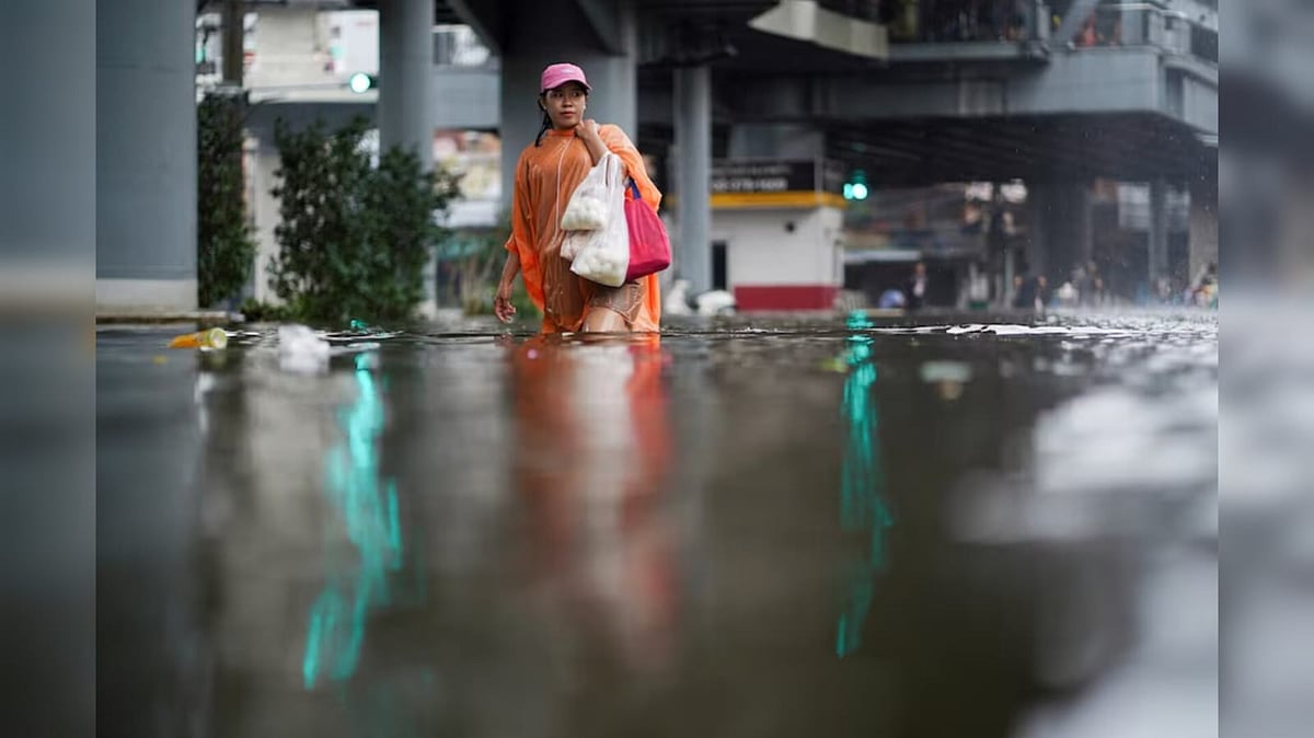 A woman carrying groceries navigate through a flooded area near a market in Bangkok - Reuters