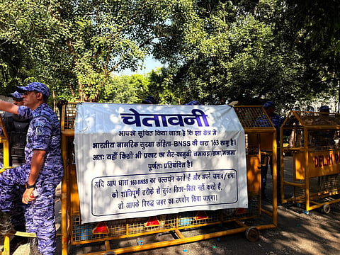 Rapid Action Force personnel stand behind barricades carrying a Hindi warning banner.
