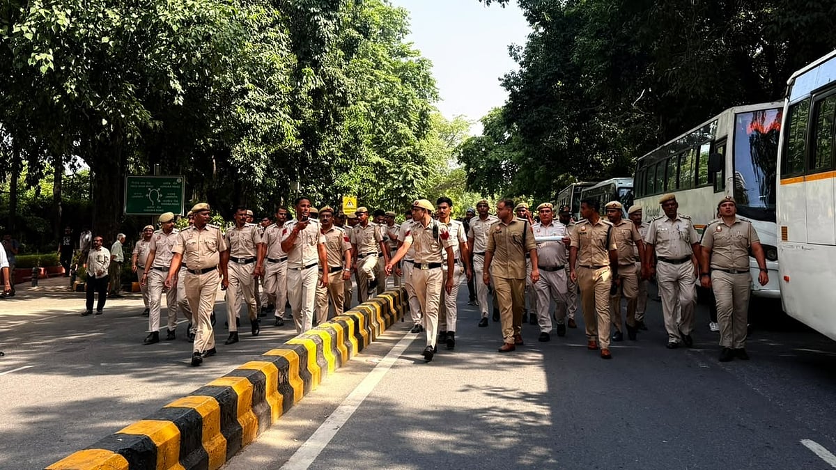 Delhi Police personnel march down a tree-lined road near Jantar Mantar on Friday, with buses parked alongside to carry away detained protesters. - null
