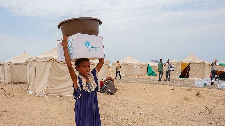 A young girl carries relief supplies on her head at a camp for displaced people in Aden, Yemen. -  | Photo: UNICEF/Mahmoud Alfilastini 