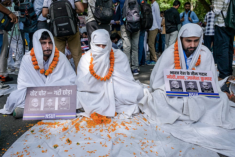 National Students' Union of India (NSUI) national president Vinod Jakhar, right, along with members wrapped in white sheets and holding placards stage a protest demanding the resignation and arrest of Chief Election Commissioner (CEC) Gyanesh Kumar over allegations of ‘vote chori’, at NSUI headquarters on Raisina Road, in New Delhi. - | Photo: PTI