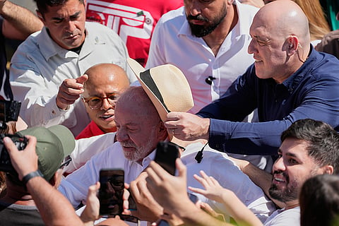 A security officer places a hat on President Luiz Inacio Lula da Silva as he leaves after voting during general elections amid a crowd in Sao Bernardo do Campo, Brazil, Sunday, Oct. 4, 2026.