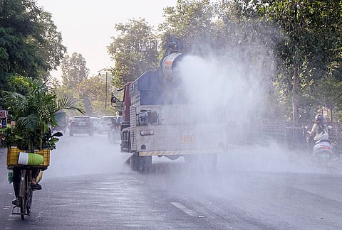 An anti-smog gun mounted on a vehicle sprays water droplets along a road to mitigate air pollution and dust levels, in Gurugram.