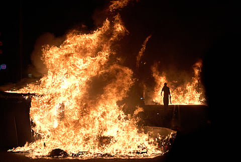 A demonstrator walks past burning trash cans set ablaze by protesters during clashes with police following a demonstration over Spain's housing crisis, hours after Prime Minister Pedro Sánchez announced an early general election, in Barcelona, Spain, Monday, Oct. 5, 2026. 
