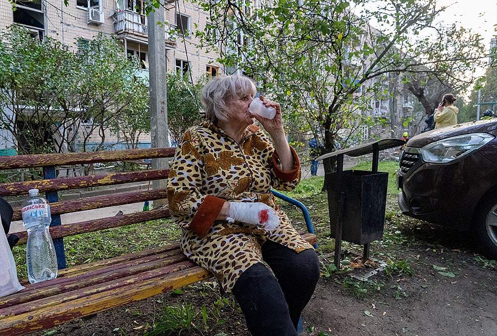 An injured woman drinks water in front of a residential house damaged by a Russian strike in Kharkiv, Ukraine, Monday, Oct. 5, 2026.  - | Photo: AP/Andrii Marienko