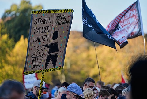 A protester holds a poster reading: "Keep the streets clean. #we are more" during a protest against the far-right AfD, Alternative for Germany, party prior to the constituent session of the new elected German federal state parliament of Saxony-Anhalt in Magdeburg, Germany, Tuesday, Oct. 6, 2026. 
