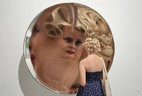 A visitor is looking in a mirror, the Inverse Reverse Perverse installation by Cerith Wyn Evans, which is displayed during a media preview of "The 90s: Art and Fashion exhibition" at Tate Britain in London, Tuesday, Oct. 6, 2026. 
