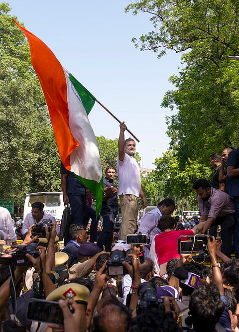 Leader of Opposition in the Lok Sabha Rahul Gandhi waves the national flag while standing atop police barricades after being stopped by security personnel during a protest march from Parliament towards the Election Commission of India (ECI) office, demanding the resignation of Chief Election Commissioner Gyanesh Kumar, in New Delhi.