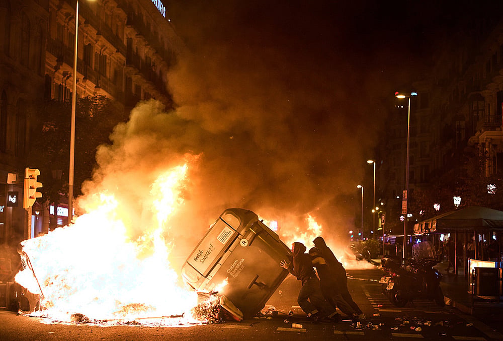 Protesters set trash cans on fire during clashes with police following a demonstration over Spain's housing crisis, hours after Prime Minister Pedro Sánchez announced an early general election, in Barcelona, Spain, Monday, Oct. 5, 2026.  - | Photo: AP/Emilio Morenatti