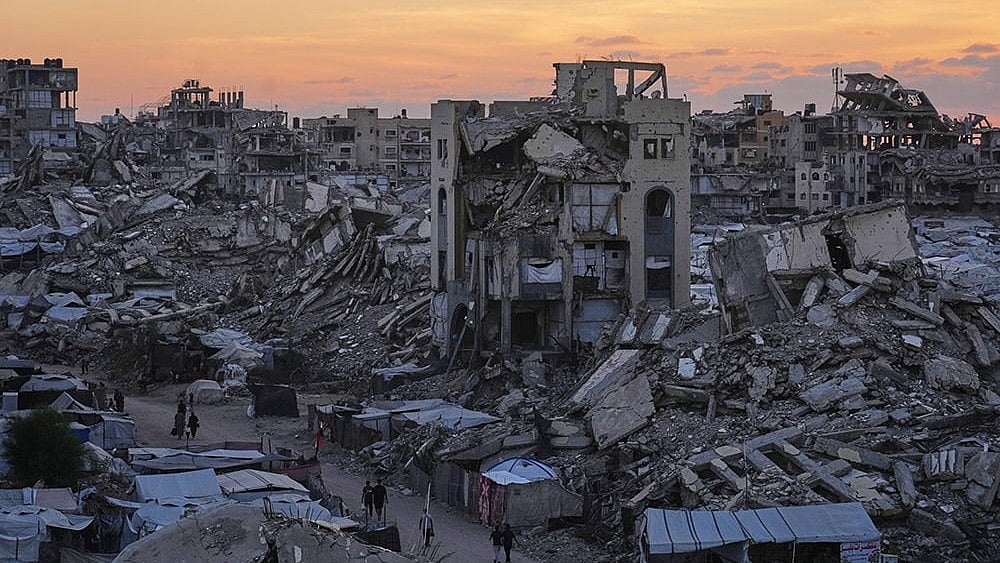 Palestinians walk amid war-damaged buildings in Gaza City. - | Photo: AP/Jehad Alshrafi