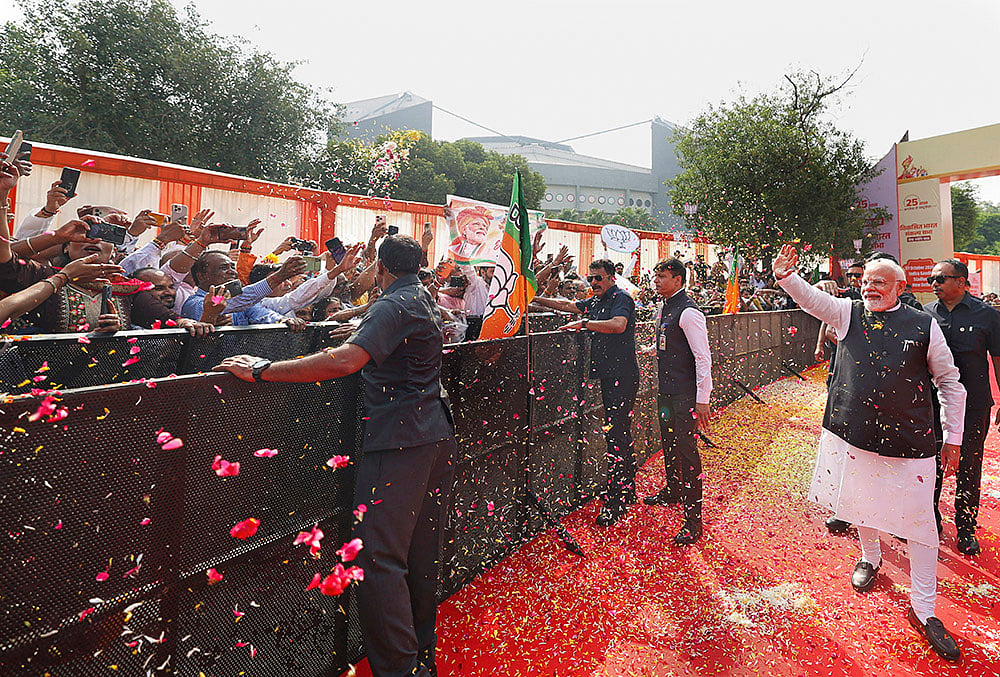 Prime Minister Narendra Modi waves to supporters during the Viksit Bharat Sankalp Sabha at the Indira Gandhi Indoor Stadium, in New Delhi. The event marks PM Modi completing 25 years as head of government in public office, tracing back to October 7, 2001, when he was sworn in as the Chief Minister of Gujarat.  - | Photo: narendramodi.in via PTI 