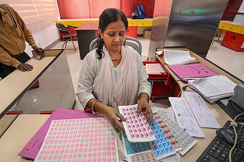 A postal official sorts and organizes sheets of postage stamps at a counter in the General Post Office (GPO) on World Post Day, in Prayagraj, Uttar Pradesh.
