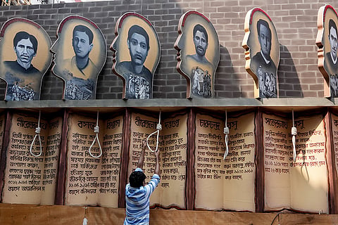A worker adjusts execution noose props beneath portraits and biographical panels honoring Indian freedom fighters at a community Durga Puja pandal, in Kolkata, West Bengal. The pandal theme brings to life key chapters of the Indian independence movement spanning from 1902 to 1945.