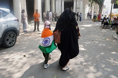 A child with the Indian flag wrapped around her walks with a burqa-clad adult as a youth demonstration demanding the resignation of the country's election chief Gyanesh Kumar is clamped down by the authorities in New Delhi, India, Saturday, Oct. 10, 2026.