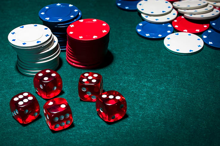 Red casino dice and stacks of poker chips on a dark felt table.