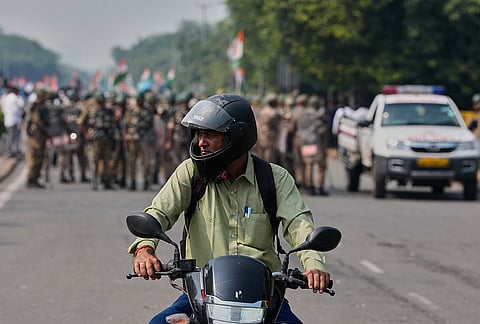 A commuter watches as security personnel arrive to escort workers of India's opposition Congress party gathering for a march toward the Supreme Court to demand the resignation of Chief Election Commissioner Gyanesh Kumar in New Delhi, India, Monday, Oct. 12, 2026. 
