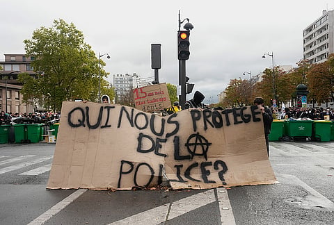 Students holds a board reading "Who protects us from the police?" as they stand in front of the Helene Boucher high school blockaded during a protest against under-resourced schools in Paris, Tuesday Oct. 13, 2026. 