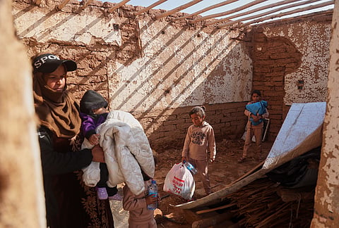 A woman holds a young child as other children carry belongings inside their damaged home after returning to Al-Arisha, in Syria's Ras al-Ayn countryside, Tuesday, Oct. 13, 2026, seven years after a Turkish military offensive alongside allied Syrian factions forced them to flee. 