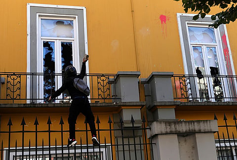 A hooded protester throws a stone toward the Education Ministry during clashes in Tirana, Albania, Tuesday, Oct. 13, 2026, joining a demonstration organized by the Flamingo protest movement demanding the resignation of Prime Minister Edi Rama. 
