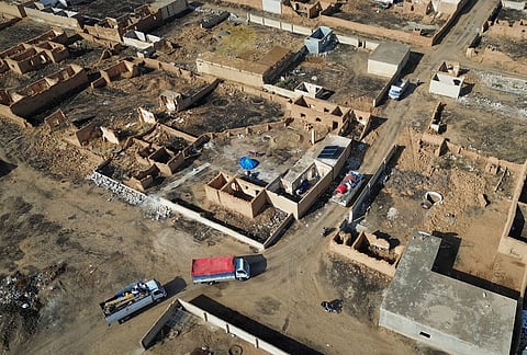 Trucks carrying returning residents and their belongings pass destroyed buildings in Al-Arisha, in Syria's Ras al-Ayn countryside, Tuesday, Oct. 13, 2026, seven years after a Turkish military offensive alongside allied Syrian factions forced them to flee. 