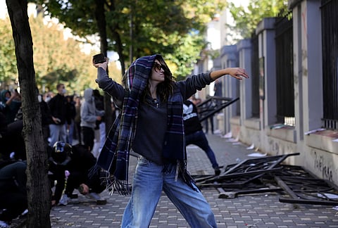 A hooded protester throws a stone toward the Education Ministry during clashes in Tirana, Albania, Tuesday, Oct. 13, 2026, joining a demonstration organized by the Flamingo protest movement demanding the resignation of Prime Minister Edi Rama. 
