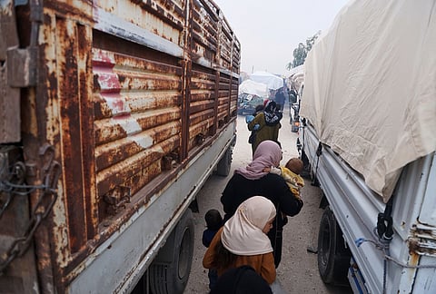 Women carry young children between trucks loaded with belongings as displaced families prepare to leave al-Talayi camp in Hassakeh, Syria, Tuesday, Oct. 13, 2026.