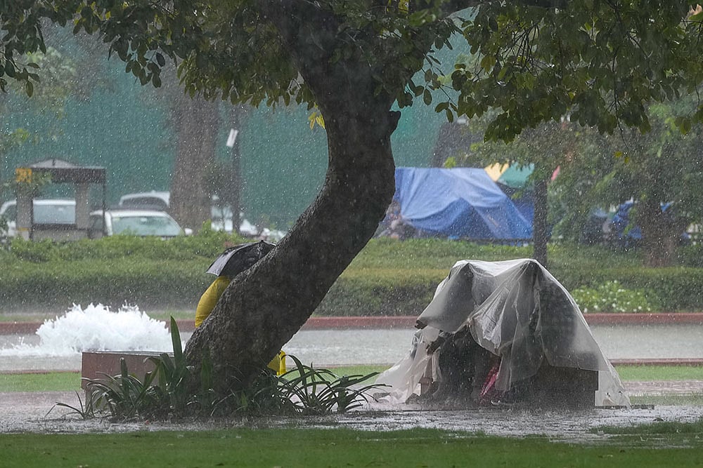 People take cover under a plastic sheet along the India Gate lawns during heavy rainfall, in New Delhi, Thursday, Oct. 15, 2026. Rain swept across Delhi on Thursday, with the skies appearing gloomy and overcast with dark clouds throughout the day, even as the India Meteorological Department (IMD) issued a red alert for moderate showers, thunderstorms, lightning and gusty winds. - | Photo: PTI/Ravi Choudhary