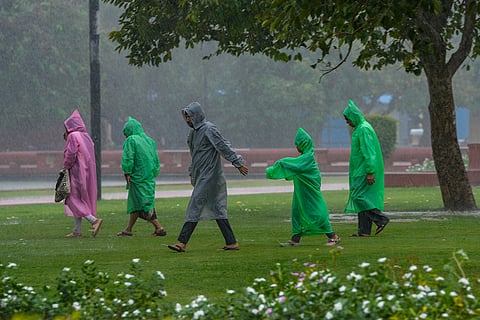 People wearing raincoats walk across a road during heavy rainfall, in New Delhi, Thursday, Oct. 15, 2026.