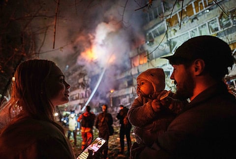Victoria Deineko, her husband Ievhen Deineko and their daughter Mia look at a multi-story residential building damaged in a Russian missile strike in Kyiv, Ukraine, Tuesday, Oct. 13, 2026. 