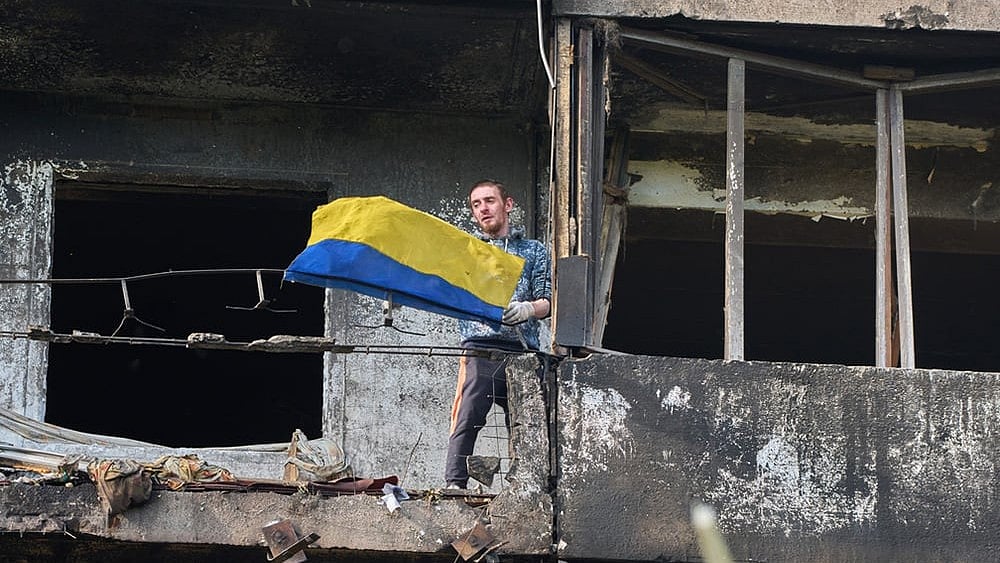 A man hangs out the national flag at his damaged apartment balcony after a missile strike during Russia's night air attack in Kyiv, Ukraine, Wednesday, Oct. 14, 2026. - | Photo: AP/Efrem Lukatsky